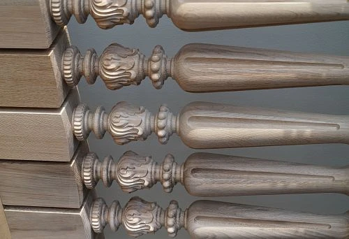 Several wooden balusters in close-up, showing delicate carving and natural wood texture.