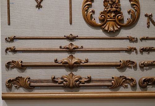 Carved wooden decorative elements of various lengths and shapes, neatly arranged on a stand, showcasing the richness of textures and styles.
