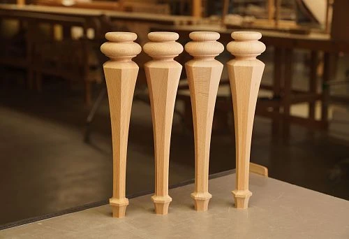 Four precisely crafted furniture legs made of solid natural wood on a workbench.