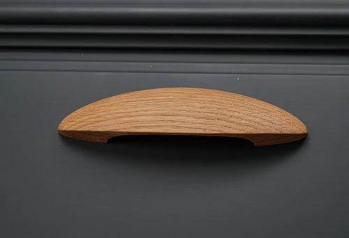 Furniture handle with ergonomic design in natural wood color.