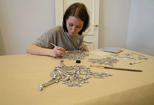 Girl manually paints a decorative carved element with silver paint
