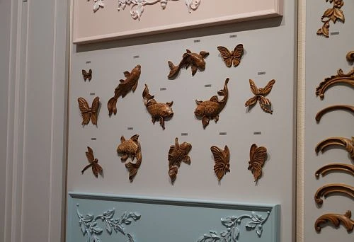 Collection of carved wooden figurines in the shape of fish and butterflies, neatly arranged on a stand with different colored panels.