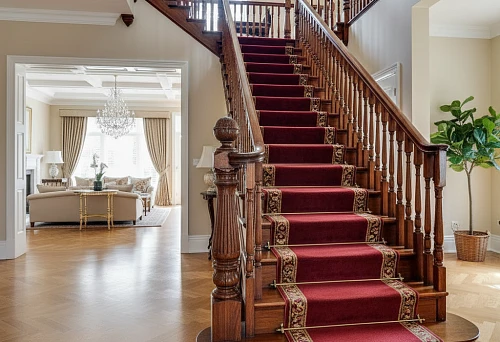 Classic wooden staircase with decorative balusters, carved posts, and burgundy carpeting in an interior with parquet flooring