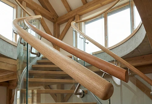 Round handrails made of oak and beech on a staircase with glass railing in wooden architecture