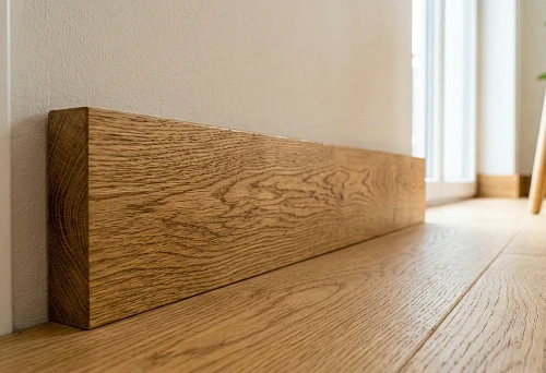 Oak wooden baseboard against a light wall: pronounced oak texture and a smooth floor joint line