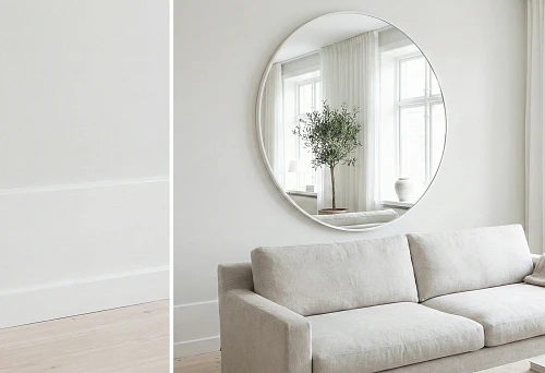Scandinavian light interior: white baseboard and white wall panel, round white mirror frame above a light sofa