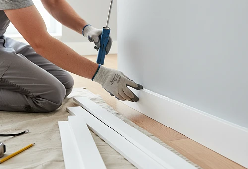 Process of installing polystyrene skirting boards yourself using a mounting gun and adhesive on the floor in a modern interior