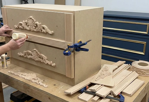 Solid wood furniture overlays: a craftsman glues carved decor onto a dresser facade in the workshop
