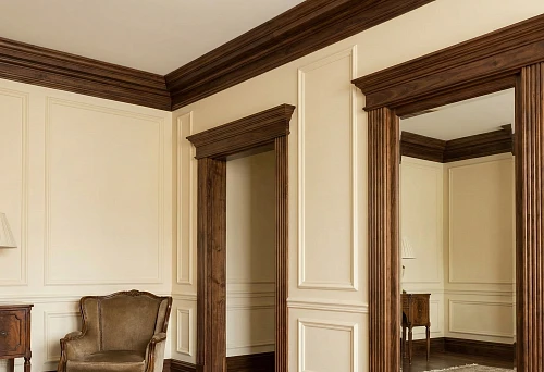 Wooden architraves and cornices in a classic interior: dark door frame trim and ceiling cornice on light walls.