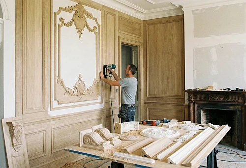 The master installs decorative overlays and moldings on a wall panel in a classic interior