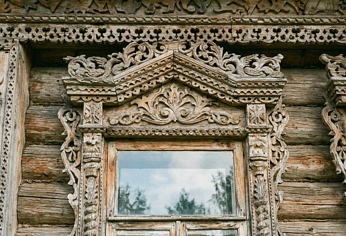 Carved window casings on a wooden house window: figured pediment, floral ornament, and house carving