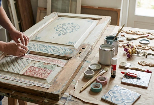 DIY door decor: a craftsman decorates an old door with a stencil and decorative inserts on a workbench