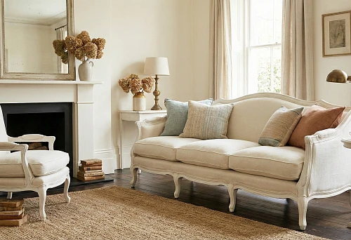 White classic living room: sofa and armchair with carved legs by the fireplace, warm textiles