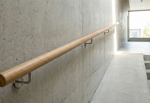 Round Wooden Wall-Mounted Handrail Along a Concrete Corridor Wall