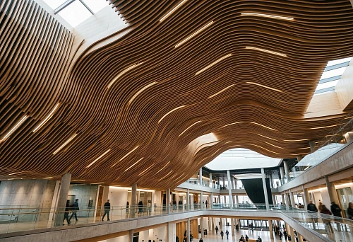 Ceiling made of slat panels in a modern public interior with wave-like architecture, built-in lighting, and a large atrium
