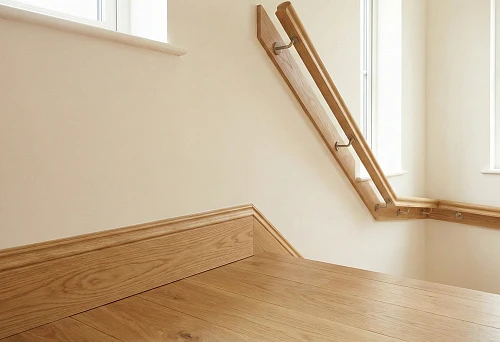 Wooden baseboard along the floor and round handrail on the staircase wall, unified interior finishing style