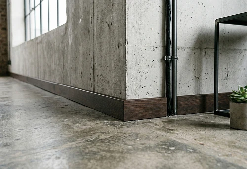 Wooden baseboard in loft style: dark flat profile along concrete wall and floor