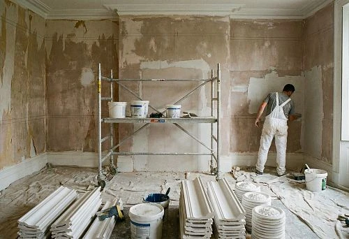 Room under renovation: worker applying leveling compound to walls