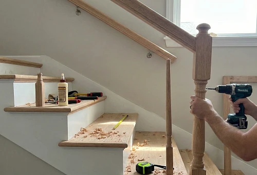 Mounting wooden balusters on a staircase, the master secures the support post and drills a mounting hole with a screwdriver