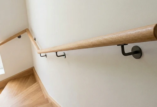 Wall-mounted round wooden handrail on brackets: secure grip along the stairs and a clean installation line