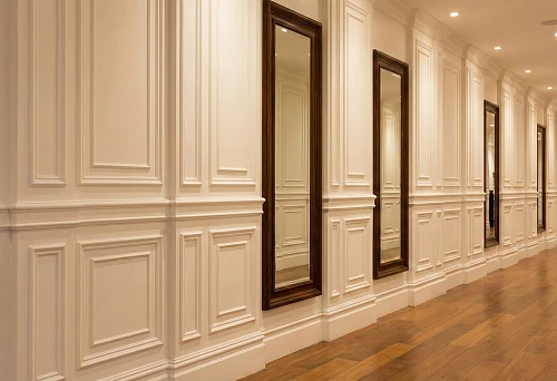 A long hallway with a high baseboard, wall moldings and framed mirrors, creating rhythm and depth in the space