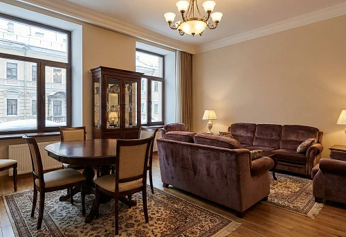 Classic living room with upholstered furniture and dining set: sofas, armchairs, round table, display cabinet, warm lighting, classic-style interior
