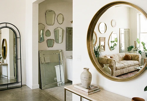 Round interior mirror in a gold frame on a light wall in the living room reflecting a soft sofa