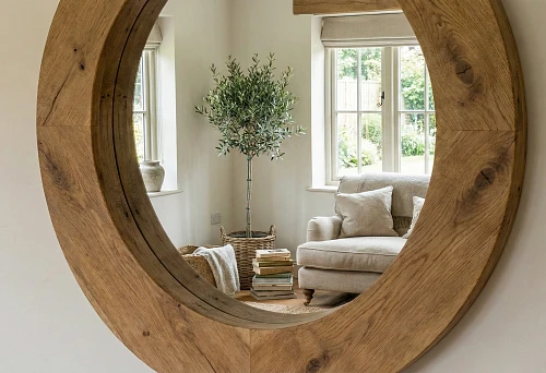 Round wall mirror with wide wooden frame, reflection of a bright room and window