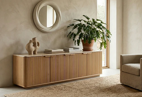 Modern wooden dresser with fluted fronts, round mirror on the wall, ceramic vase, and large plant by the window
