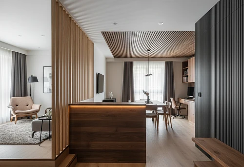 Interior with zoning using wooden slats, panels, and millwork, dividing the space of the living room, kitchen, and work area