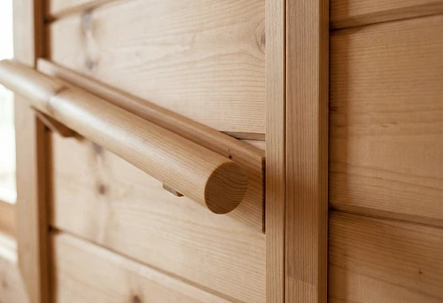 Round solid wood handrail on the interior side of a wooden wall, close-up