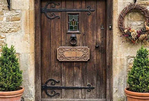 Decorating a Wooden Door with a Carved Overlay: Decorative Panel on the Door Leaf, Forged Hinges, and Stone Facade