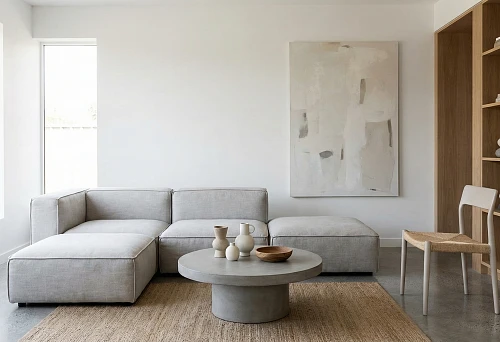 Minimalist living room with a gray modular sofa, round concrete coffee table, jute rug, and abstract painting