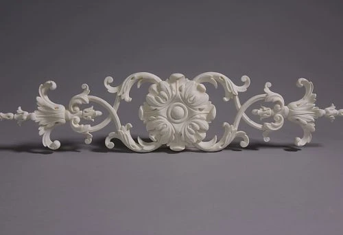 Classic molding decoration element with central rosette and symmetrical scrolls, executed in light tone on gray background.