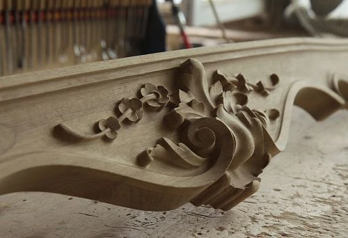 Handcrafted oak carved element with a large leaf ornament, set against a workshop background