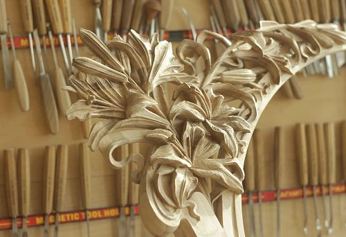 A carved oak element with an exquisite floral pattern, handmade, against a backdrop of workshop tools.