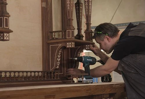A craftsman working on carved furniture made of natural wood, using power tools