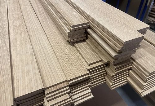 Wooden sticks with smooth surface and profiled shape, neatly stacked on a production table