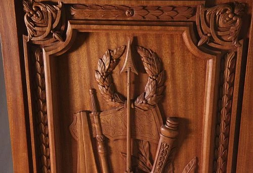 Wooden decorative relief with spear, wreath, and weapon elements in classical style