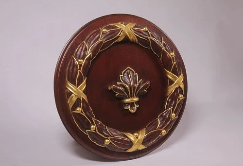 Round wooden relief with carved laurel wreath and central element in the form of a golden lily, executed in the technique of artistic stucco.