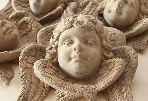 Carved angel head sculpture with wings, handcrafted from oak, with detailed rendering of the face and feathers.