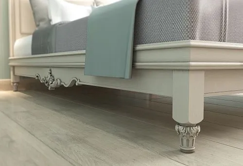 Lower part of the bed with carved decoration on legs in a light interior