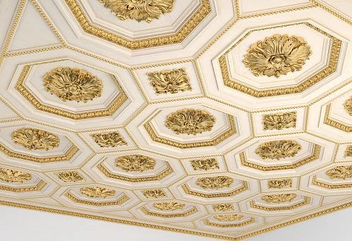 White ceiling with gold molded decoration and complex geometry in a wooden house.