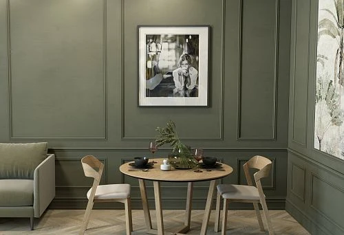 Round solid wood table with designer chairs in an elegant green interior