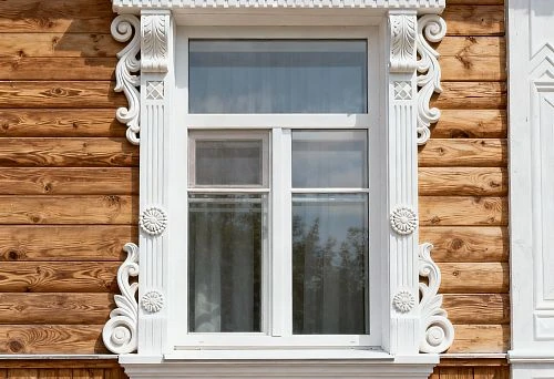 Facade decoration for exterior window cladding on a wooden house with white carved elements