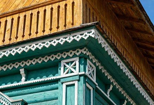 Terem facade of a wooden house with carved white window frames, battens and corner elements against a green log wall background