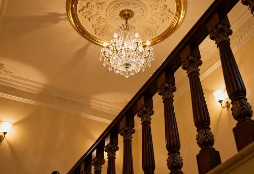 Ceiling rose under the chandelier and rhythm of wooden balusters in a classic interior