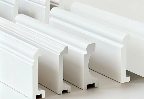 White skirting boards and cornices of various profiles, made from polystyrene and duropolymer, shown in close-up for comparing shape and material.