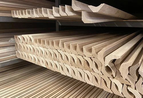 Stack of unpainted wooden moldings with deep profiled shapes, neatly arranged on a warehouse shelf