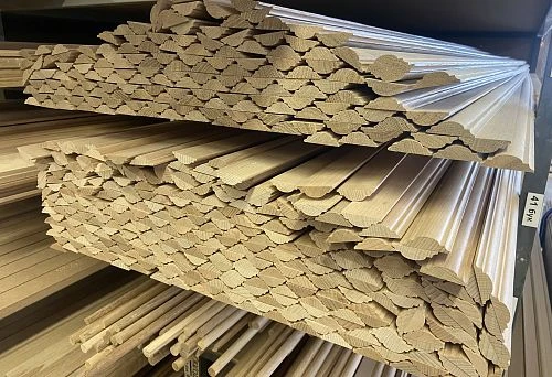 Stack of unfinished solid wood bагетs with decorative profile, neatly arranged in the warehouse